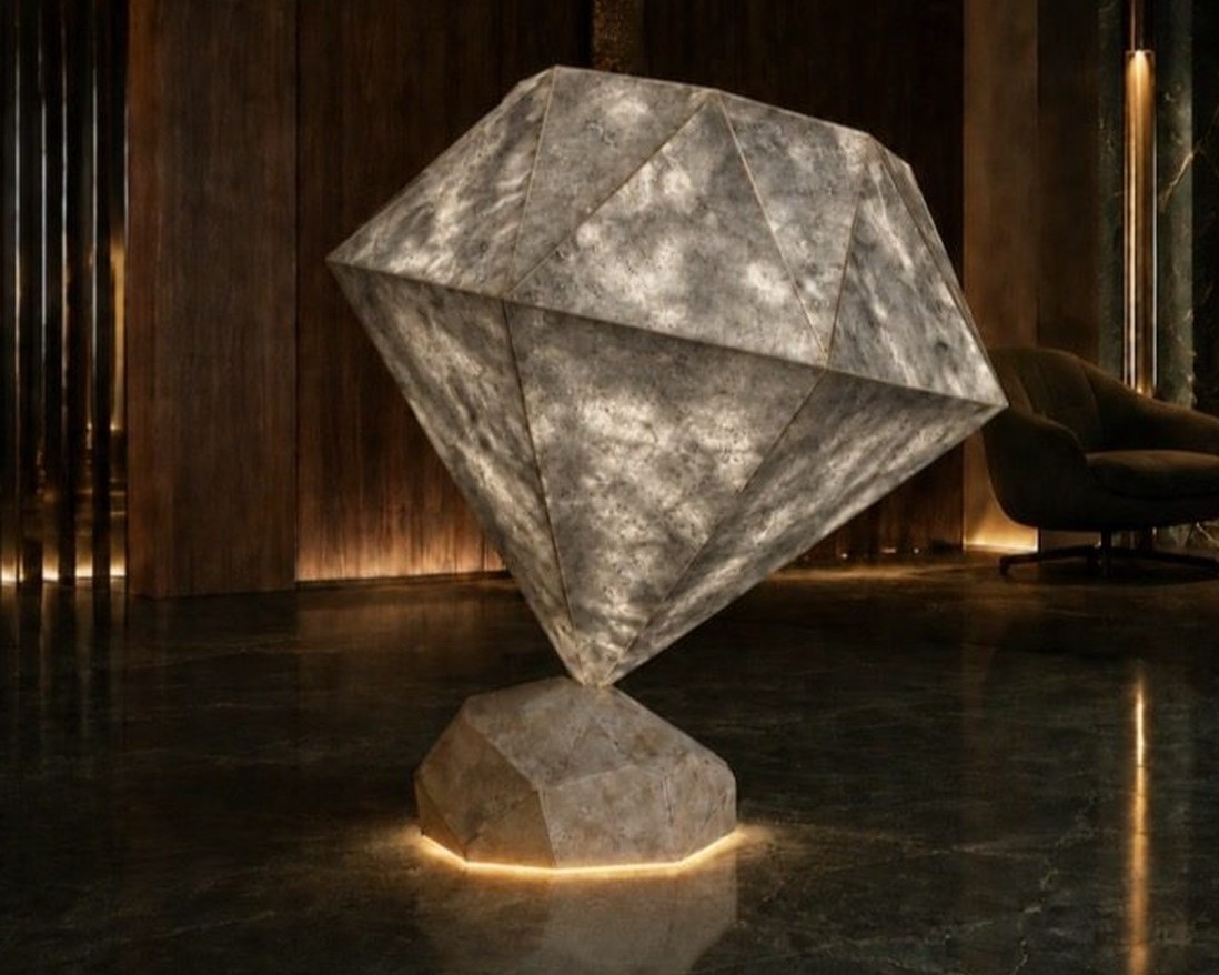 Équilibre Minéral, sculpture en travertin gris posée en équilibre sur son socle, rétroéclairée dans un hall la nuit
